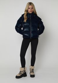 Giacca puffer blu navy con colletto alto, chiusura con zip e tasche applicate. Paio di leggings neri e stivali foderati in pelliccia color beige con suola robusta.
