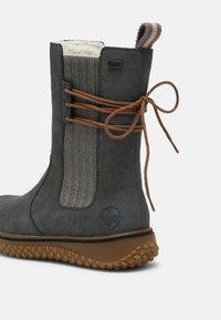 Hallitus- ja veekindel hall saabas, millel on herringbone kangast paneel, pruunad paelad ja tekstureeritud kummist tald. Küljel on logo.