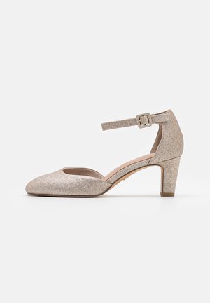 Chaussure beige pailletée à talon bas, bout pointu fermé, bride à la cheville avec boucle et talon bloc sur fond blanc.
