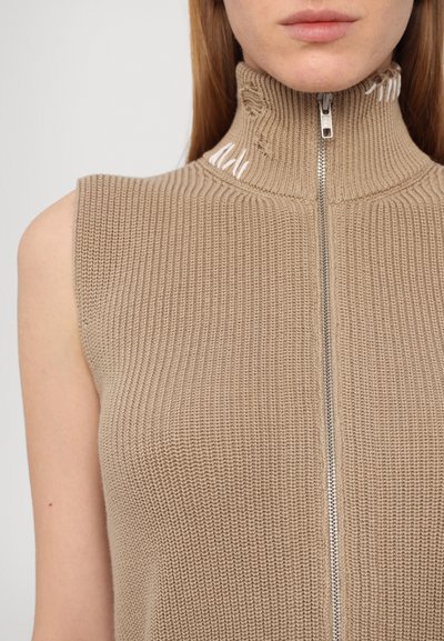 Beige sleeveless knit top with a high collar, featuring a front zipper and subtle distressed accents at the collar. Textured ribbed design.