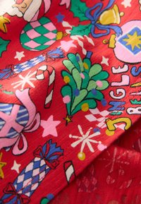 Tissu rouge avec un motif festif comprenant des cannes en sucre d'orge, des ornements de Noël, des feuilles de houx et des étoiles de différentes couleurs et formes.