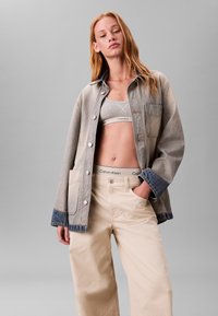 Spijkerjack in lichtgrijs met knoopsluiting, grote voorkantzak en donkerblauwe manchetten, gecombineerd met beige wijde broekspijpen en een grijze cropped top.