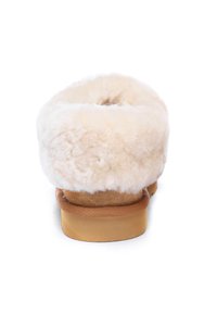Soft, cream-colored slipper with a fluffy, textured wool upper and a tan suede base. Rounded shape and cushioned sole for comfort.