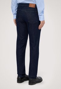 Mörkblå denimjeans med rak benpassning. Har bakfickor och en brun läderetikett på midjan. Slät textur.