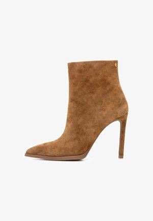 Beżowe zamszowe botki za kostkę z zakończeniem w punkt, 10-centymetrowym obcasem typu stiletto oraz minimalistycznym designem. Dyskretne detale z logo po bokach.