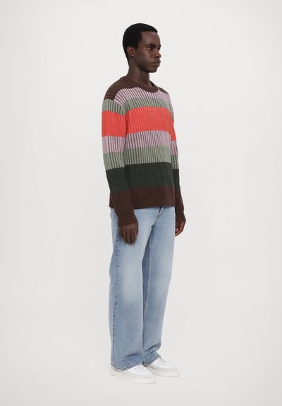 Multicolored knitted sweater featuring horizontal stripes in shades of brown, green, pink, and orange. Paired with light blue jeans and white shoes.