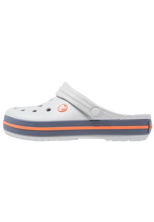 Biały chodak z otworami wentylacyjnymi, granatowo-pomarańczowa paskowana podeszwa, lekka konstrukcja oraz pasek dla pewnego dopasowania. Obecne logo marki Crocs.