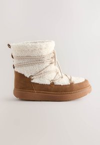Botte en daim beige et fausse fourrure crème, avec lacets beige, bout rond et semelle en caoutchouc texturée ; elle présente des œillets en métal et un col moelleux.