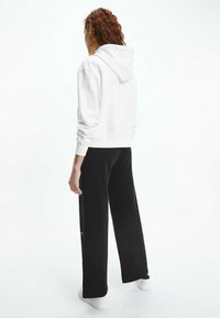 Sudadera blanca con cordón, combinada con pantalones de chándal negros de corte holgado. Zapatillas blancas visibles, de diseño simple y textura suave.