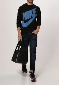 Černá mikina s velkým modrým logem "Nike", tmavě modré džíny, šedé tenisky s červenými akcenty a černá taška přes rameno se stříbrnými detaily.