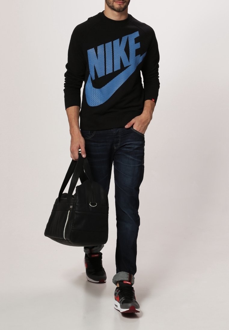 Černá mikina s velkým modrým logem "Nike", tmavě modré džíny, šedé tenisky s červenými akcenty a černá taška přes rameno se stříbrnými detaily.