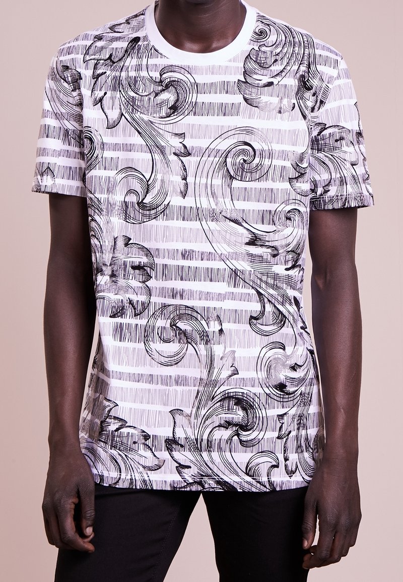 T-shirt à manches courtes noir et blanc avec des motifs floraux tourbillonnants sur des rayures horizontales. Fabriqué en tissu léger avec un col rond.