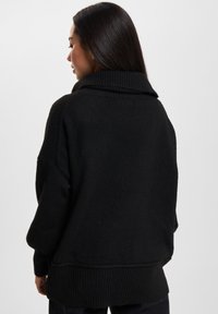Svart oversized genser med høy krage og ribbet tekstur. Har vide ermer og en løs passform, som gir et koselig utseende.
