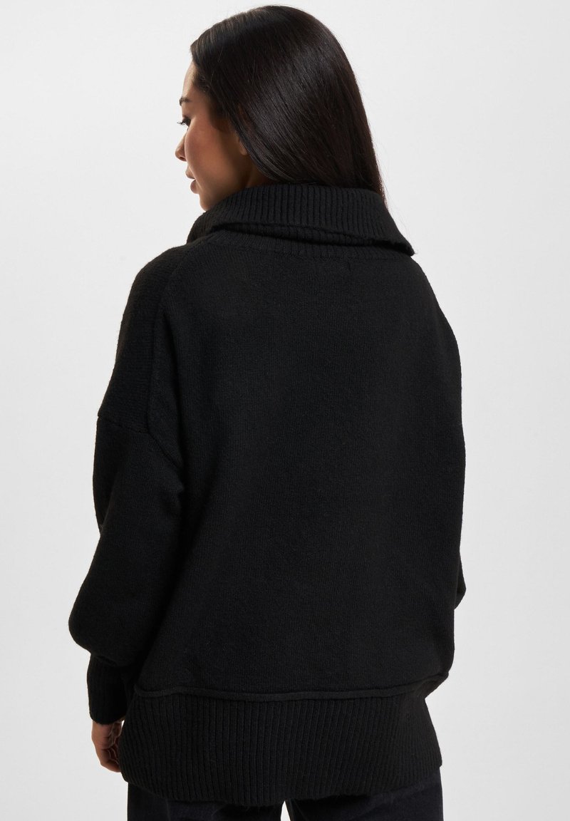 Czarny, oversize sweter z wysokim kołnierzem i prążkową teksturą. Posiada szerokie rękawy i luźny krój, co zapewnia przytulny wygląd.