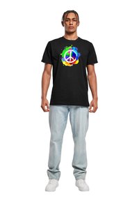 Sort bomulds t-shirt med et farverigt fredstegn grafik omgivet af livlige malingsplasker. Kombineret med lyseblå denim jeans.