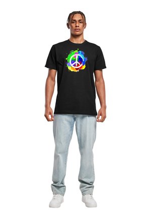 Schwarzes Baumwoll-T-Shirt mit einem bunten Friedenssymbol-Grafik, umgeben von lebhaften Farbspritzern. Kombiniert mit hellblauen Jeans.