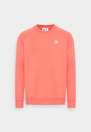 Korallinvärinen Adidas-collegepaita, jossa on pitkät raglanhihat ja pieni valkoinen Adidas Trefoil -logo vasemmalla rinnalla.