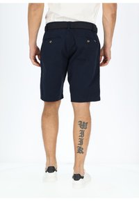 Navy shorts made of cotton with a smooth texture, featuring two back pockets with buttons and a woven black belt. White sneakers complete the look.