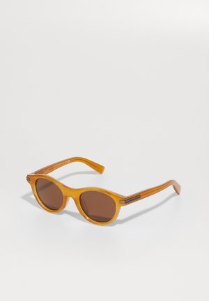 Round sunglasses with a translucent orange frame, dark brown lenses, and sleek, striped arms featuring silver-tone accent hardware.