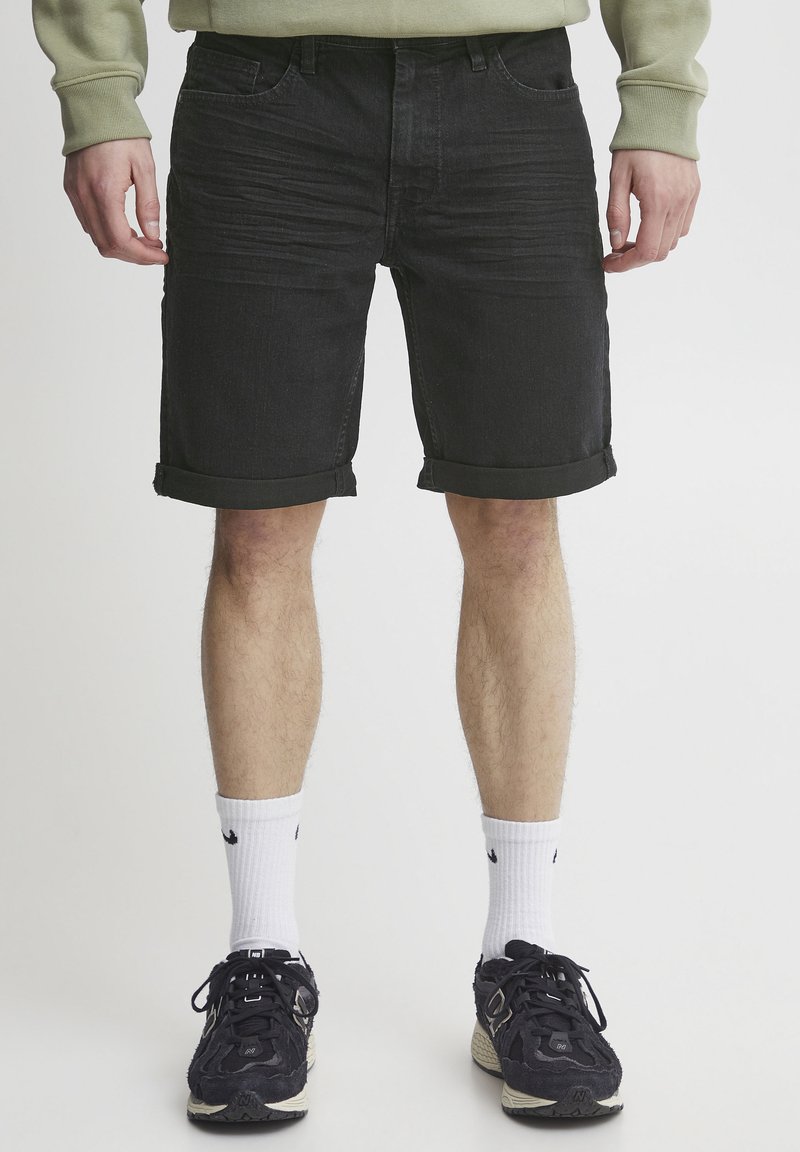 Sorte denimshorts med rullekanter, med frontlommer og en teksturert overflate. Kombinert med hvite sokker og svarte joggesko.
