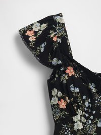 Zwart bloemig jurkje met ruches korte mouwen en kantafwerking langs de halslijn, versierd met roze, blauwe en witte bloemen en groene bladeren.