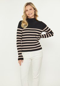 Pulover cu guler înalt, cu dungi negre și crem, dintr-un material texturat cu caneluri, având mâneci lungi și un design ajustat, asortat cu pantaloni albi.