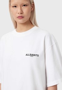 Λευκό βαμβακερό t-shirt με στρογγυλή λαιμόκοψη και κοντά μανίκια, με μαύρο τυπωμένο λογότυπο "ALLSAINTS LONDON" στο αριστερό στήθος.