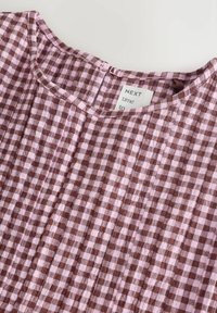 Material maro și roz cu model în carouri gingham și textură plisată, având o decolteu rotund și o etichetă pe care scrie "NEXT time to."