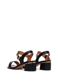 Zwarte hakken sandalen met een elegant ontwerp, brede crossoverbanden, een goudkleurige accent op de hak en een textured zool.