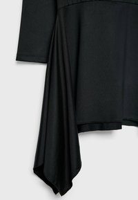 Vêtement noir à manches longues avec un ourlet asymétrique comportant un large panneau de tissu drapé suspendu d'un côté.