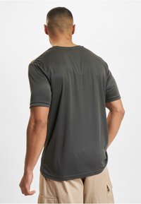 Czarnoszary t-shirt z krótkim rękawem, wykonany z teksturowanej tkaniny, z okrągłym dekoltem i subtelnymi detalami szwów, noszony z jasnobeżowymi szortami cargo.