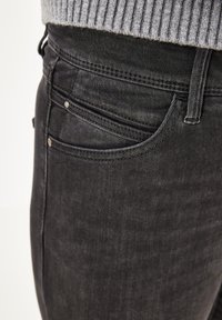 Schwarze Denim-Jeans mit einem klassischen Fünf-Taschen-Design, subtilen Verwaschungen und Metallnieten. Der Stoff hat eine glatte, leicht strukturierte Oberfläche.
