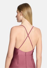 Femme aux cheveux blonds raides portant une robe mauve sans manches avec des bretelles fines croisées et un dos décolleté.