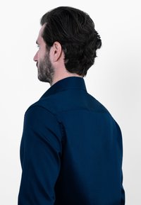 Marineblauw overhemd met knopen, zachte textuur, getailleerde pasvorm, standaardkraag, zichtbare stiksels, gedragen door een man gezien vanuit de rug.