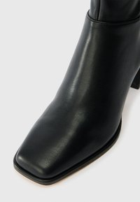 Black leather ankle boot with a square toe and block heel. Smooth texture, minimal stitching, and a polished finish.