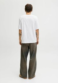 Hvid bomulds t-shirt med korte ærmer, parret med løstsiddende, falmede olivenfarvede bukser og lysebrune flade sko.