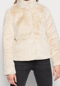 Cream-colored faux fur jacket with a high collar, button closure, and soft texture. Features wide sleeves and a boxy silhouette.