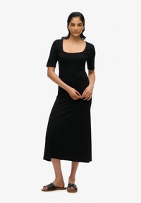 Robe noire, ajustée, longueur cheville avec un décolleté carré et des manches courtes ; associée à des sandales noires à glisser avec un design tissé.