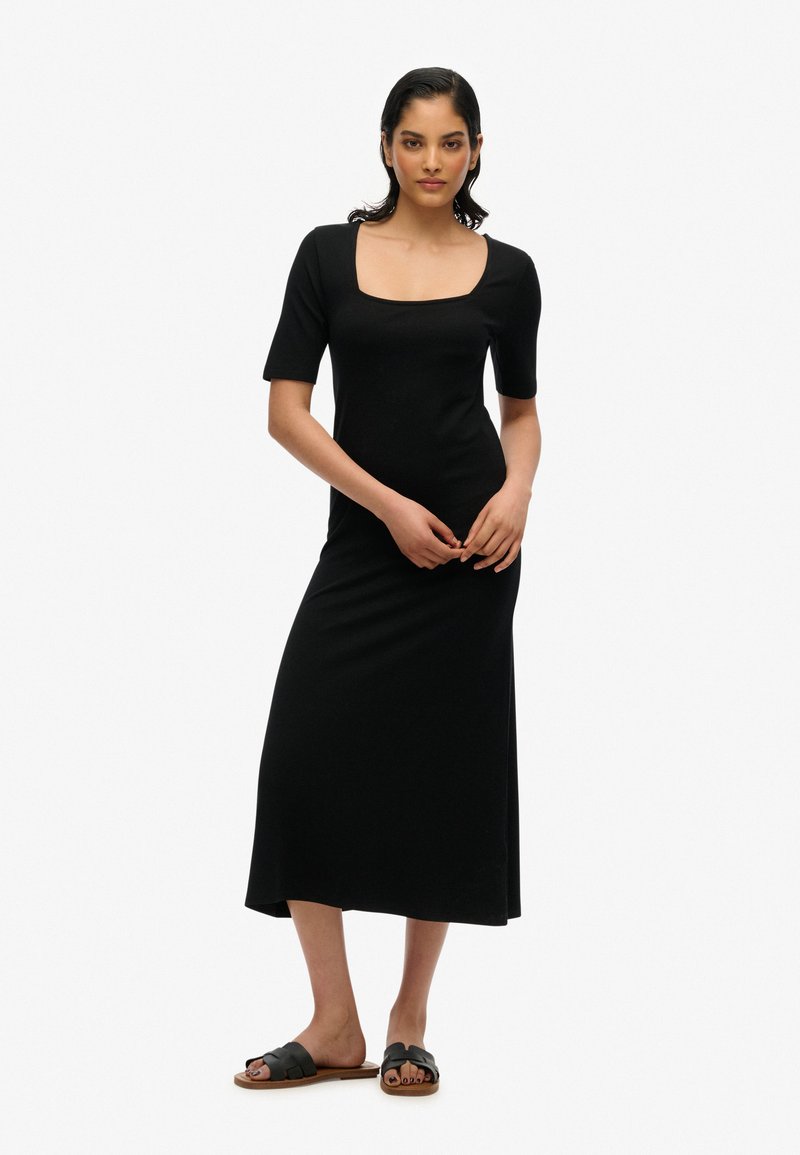Robe noire, ajustée, longueur cheville avec un décolleté carré et des manches courtes ; associée à des sandales noires à glisser avec un design tissé.