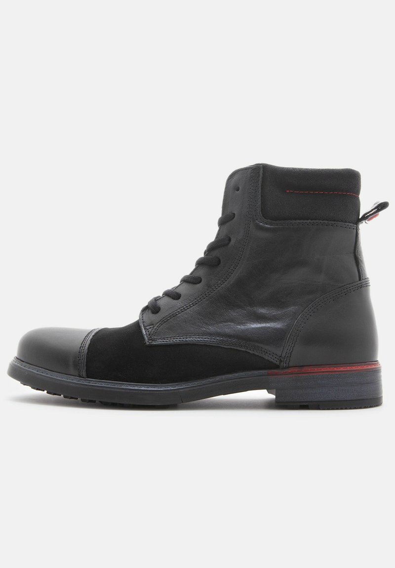 Botín negro con parte superior de cuero liso y acentos de ante. Presenta una puntera redonda, diseño con cordones y un acento rojo en la suela.