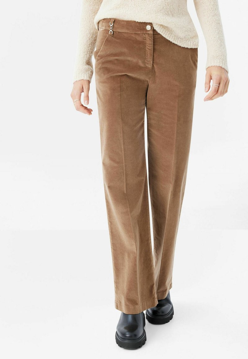 Bruna kordflodbyxor med rak passform, försedd med en främre dragkedjeficka, knäppning och subtil textur. Matchas med svarta skor.
