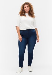Jeans ajustados de color azul oscuro combinados con una blusa de manga corta blanca, que presenta un diseño ajustado y una textura suave, complementados con zapatillas blancas.