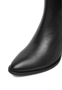 Bocanc de piele neagră până la gleznă, cu vârf ascuțit și textură netedă. Dispune de un design elegant și un toc subțire, curbat.