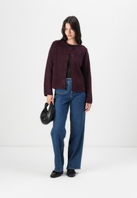 Bordeaux ullblandede cardigan med rund hals, frontknapper, lange ermer, kombinert med blå vide jeans og en svart veske.