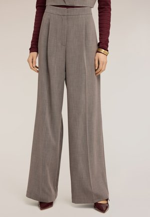 Pantalon gris taille haute à jambes larges porté avec des escarpins bordeaux à bout pointu et un haut bordeaux à manches longues, accessoirisé de bracelets en or.