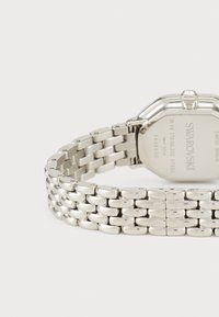 Silberner Edelstahl-Uhr mit einem achteckigen Ziffernblatt und einem strukturierten Gliederarmband. Verfügt über einen kleinen Kristall auf der Krone und eine gravierte Rückseite.