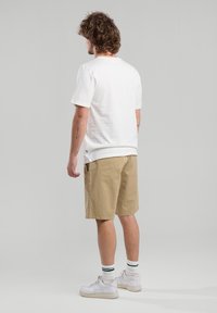 Valkoinen lyhythihainen t-paita, vaaleat shortsit, valkoiset tennarit, vihreäpaitaiset sukat; yksinkertainen muotoilu, rento istuvuus, puuvillamateriaali.