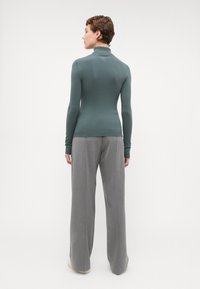 Langermet, teal turtle neck genser kombinert med lysegrå, vide bukser. Myk tekstur, tettsittende design og subtile ribbestrikkdetaljer.