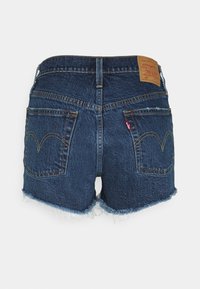 Pantalones cortos de mezclilla azul oscuro con dobladillos deshilachados, bolsillos traseros clásicos y una etiqueta de marca Levi's marrón en la cinturilla.