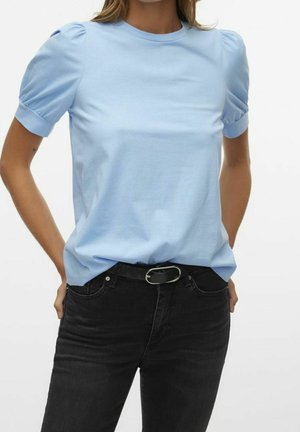 Kvinde iført en lyseblå t-shirt med pufærmer stoppet ned i højtaljede sorte jeans med sort bælte.